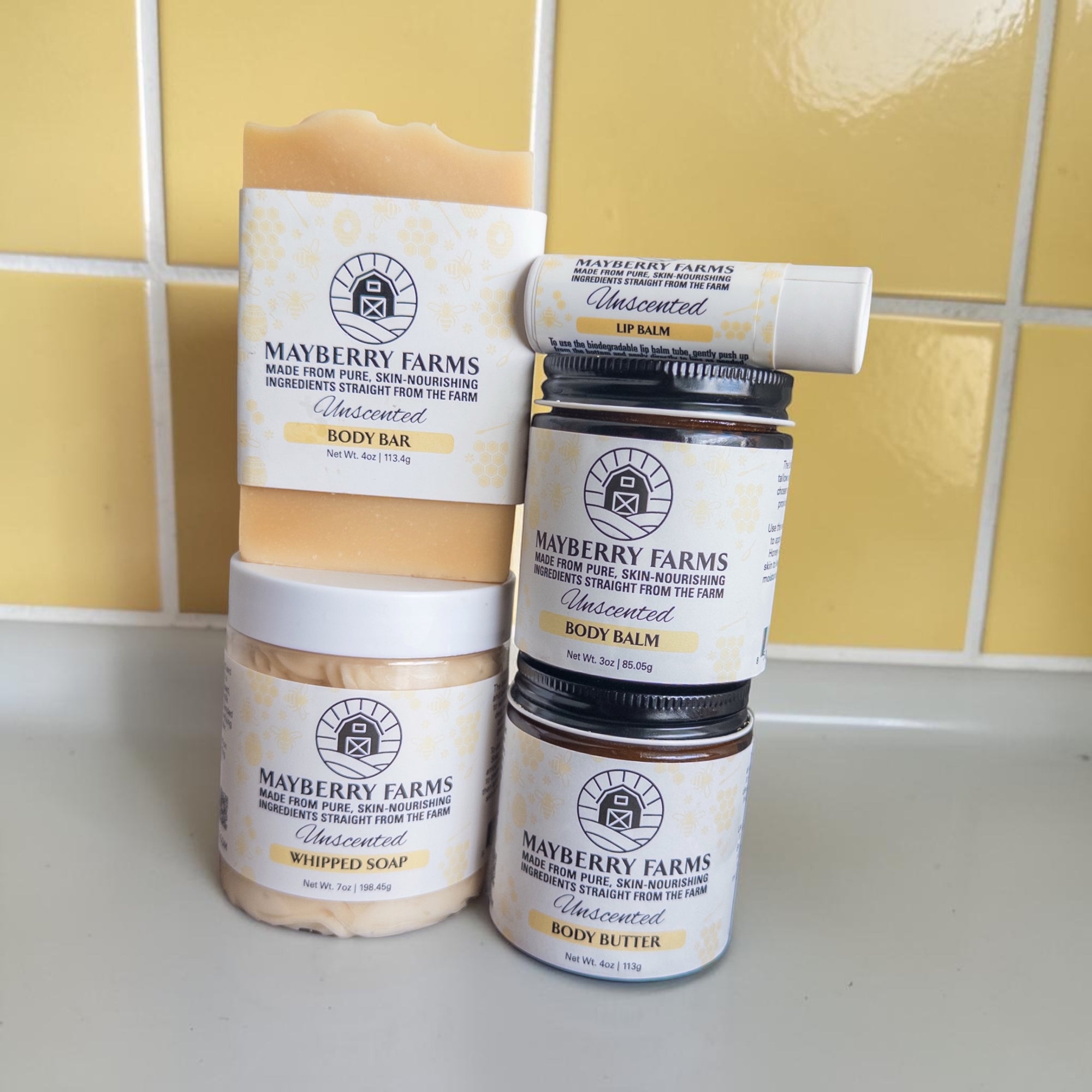 Collection of Mayberry Farms skincare products on a tiled bathroom counter.
