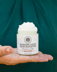 Person holding a jar of Mayberry Farms body balm against a green background