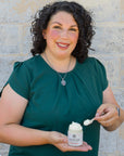 Woman holding a jar of cream and a applicator against a brick wall.