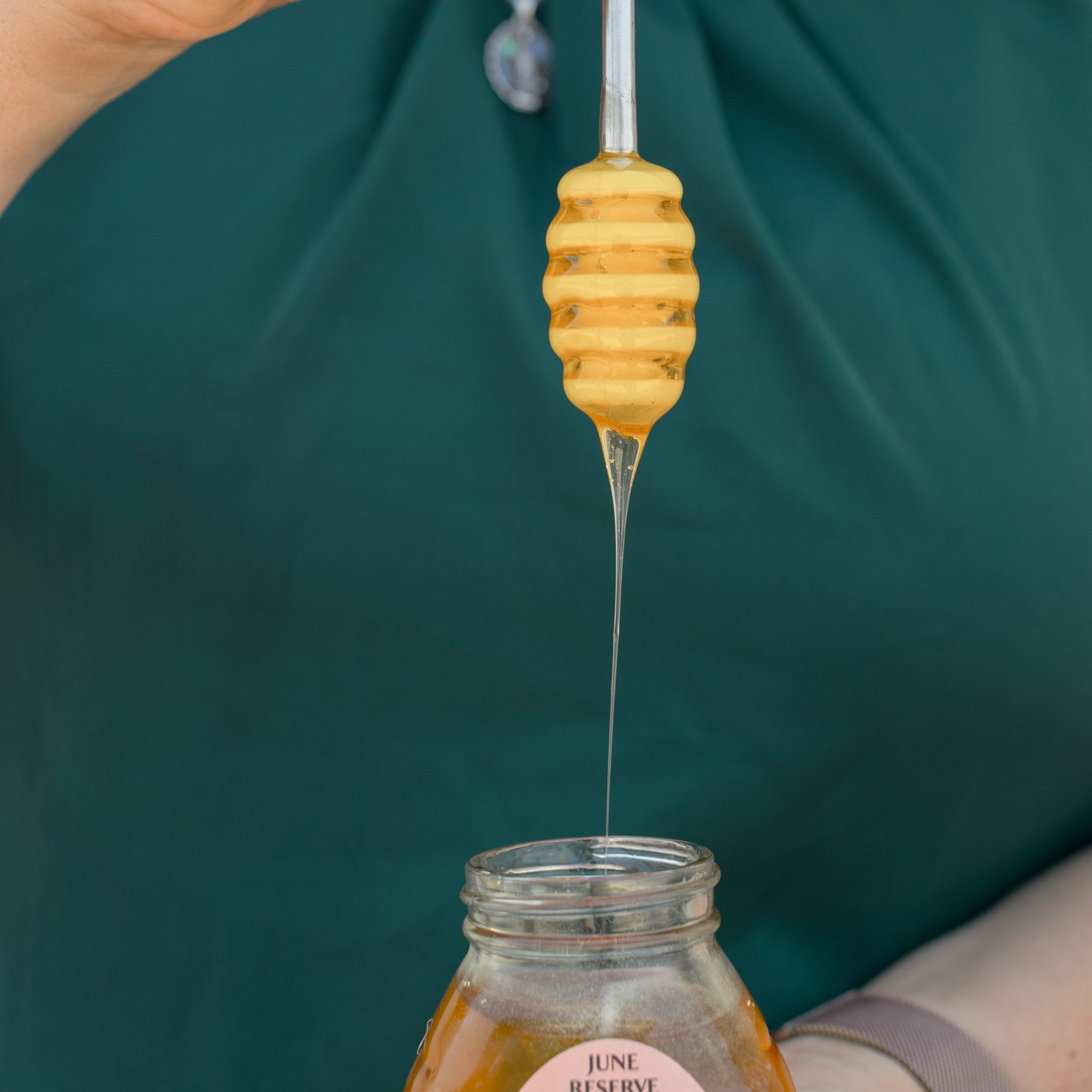 Person using a honey dipper to draw honey from a jar.