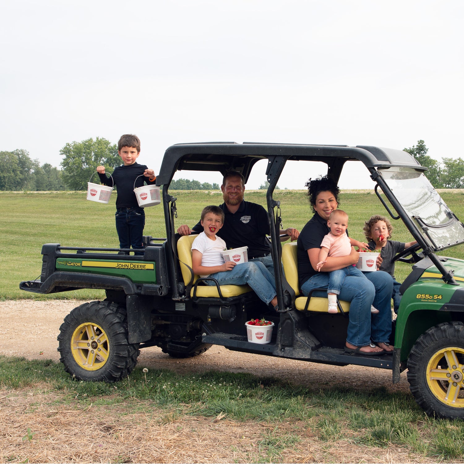 Tim and Danielle Clark plus kids sitting on John Deere Gator in the field with strawberries